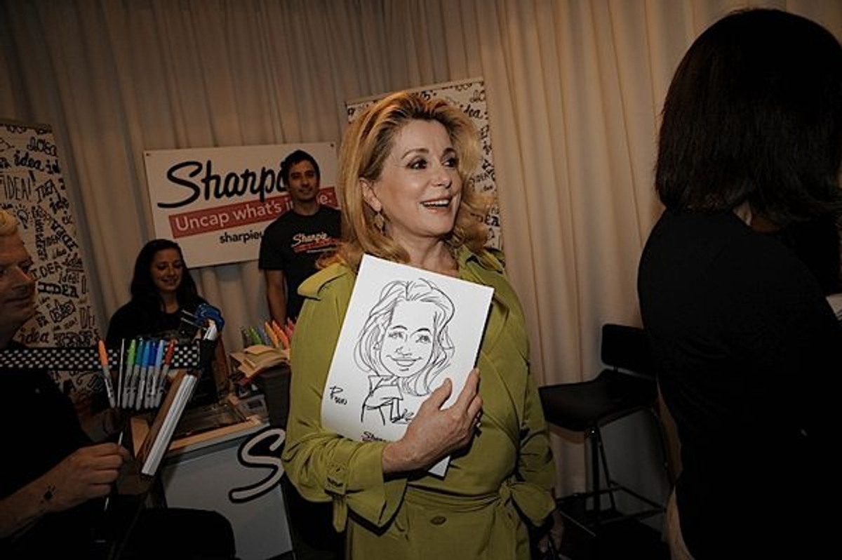Catherine Deneuve poses with a charicature of herself at the Sharpie booth in the IT Lounge.