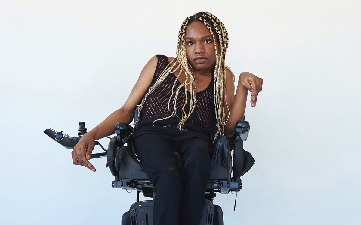 Model Aaron Rose Philip pictured here wearing a black top and pants while sitting in a wheelchair